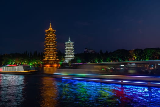 Tourist boats sailing in front of illuminated at night Sun and Moon Pagodas Towers at Shanhu or Shan Lake in Guilin town, Guangxi Province, China