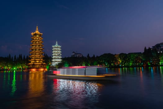 Tourist boats sailing in front of illuminated at night Sun and Moon Pagodas Towers at Shanhu or Shan Lake in Guilin town, Guangxi Province, China