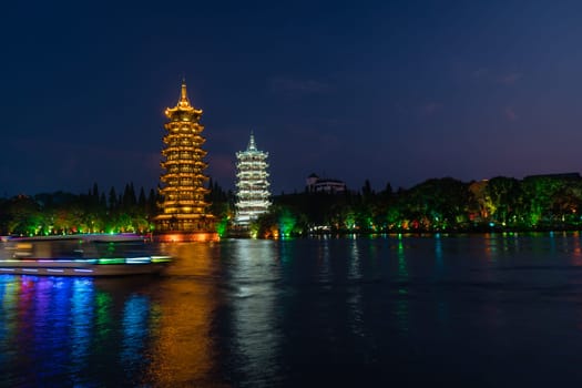 Tourist boats sailing in front of illuminated at night Sun and Moon Pagodas Towers at Shanhu or Shan Lake in Guilin town, Guangxi Province, China