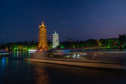 Tourist boats sailing in front of illuminated at night Sun and Moon Pagodas Towers at Shanhu or Shan Lake in Guilin town, Guangxi Province, China