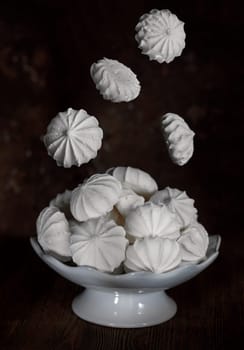 White meringues in a white porcelain vase on a dark brown background, with flying meringues on top, levitation