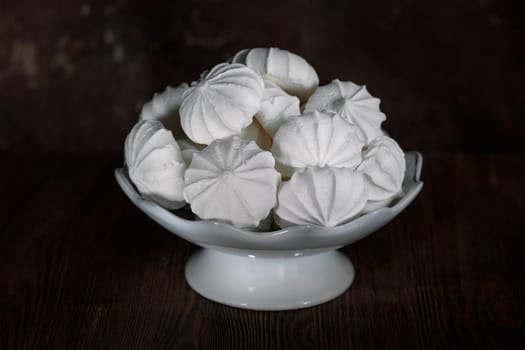 White meringues in a white porcelain vase on a dark brown background