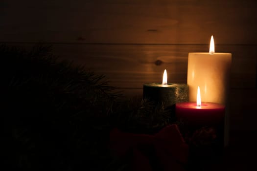 Three burning candles, red, green and white surrounded by darkness with copy space on left hand side of image