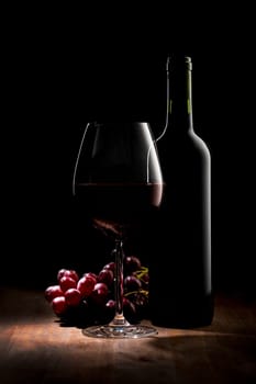 Elegant bottle of red wine with wine glass and grapes. Low key image with copy space at top left.