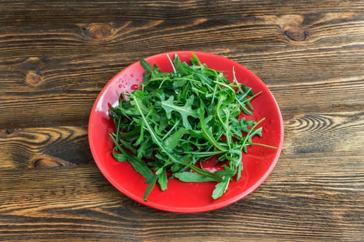 arugula lettuce on a red plate on a wooden background