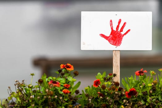 Shield with painted red hand stands in a flowerbed with copy space and blurred background