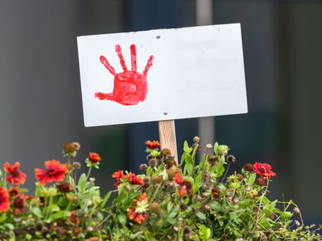 Shield with painted red hand stands in a flowerbed with copy space and blurred background