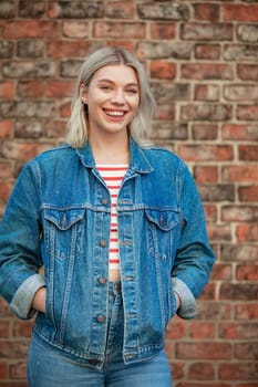 A woman standing in front of a brick wall and looking into the camera while smiling.