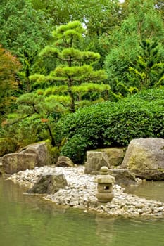 A tranquil scene with rocks, a rock lantern, water and trees in the japanese garden in Augsburg, Germany
