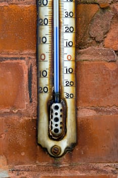 Close up of an old weatherd white enamel thermometer on a factory brick wall.With both fahrenheit and celsius scales