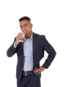 A young east Indian man standing in his suit with a glass of water, .looking into the camera and drinking, isolated for white background.