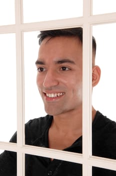A happy east Indian man standing behind a white window frame in a.black dress shirt with a big smile, isolated for white background.