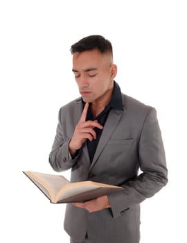 A young handsome east Indian man standing in a gray suit with a.book in his hands, reading, isolated for white background.