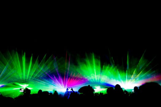 Luxury entertainment with audience silhouettes in nightclub event, festival or New Year's Eve. Beams and rays shining colorful lights.