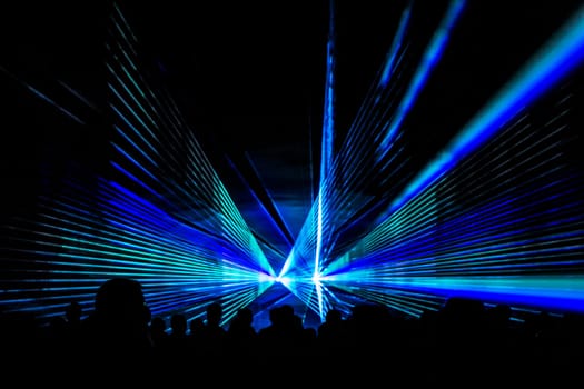 Luxury entertainment with audience silhouettes in nightclub event, festival or New Year's Eve. Beams and rays shining colorful lights.