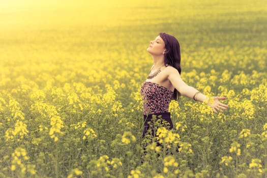 Attractive young beauty girl enjoying the warm sunny sun in nature rapeseed field takes time feeling sustainability and contemplation.