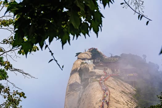 Huashan, China -  August 2019 : Crowds of tourists walking on a narrow ridge on a mountain trail to the West Peak on Huashan mountain, Xian, Shaanxi Province