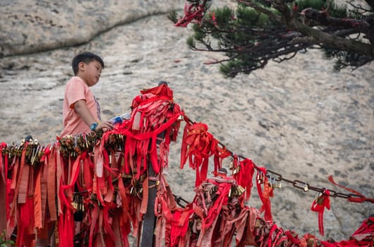 Huashan, China -  August 2019 : Chinese boy standing under small tree and posing for photos on a narrow ridge on a mountain trail from West to South Peak on Huashan mountain, Xian, Shaanxi Province