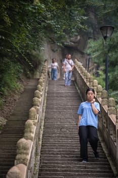 Huashan, China -  August 2019 : Chinese woman standing on the stairs on a steep mountain trail to the North and West Peak on Huashan mountain, Xian, Shaanxi Province