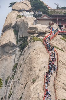 Huashan, China -  August 2019 : Crowds of tourists walking on a narrow ridge on a mountain trail to the West Peak on Huashan mountain, Xian, Shaanxi Province