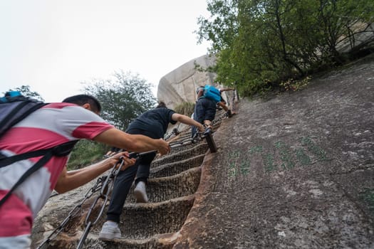 Huashan, China -  August 2019 : Tourists climbing up the vertical, steep, cut into rocky edge stairs on a mountain trail to the North and West Peak on Huashan mountain, Xian, Shaanxi Province