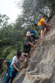 Huashan, China -  August 2019 : Tourists climbing up the vertical, steep, cut into rocky edge stairs on a mountain trail to the North and West Peak on Huashan mountain, Xian, Shaanxi Province