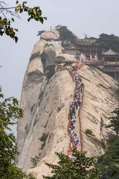 Huashan, China -  August 2019 : Crowds of tourists walking on a narrow ridge on a mountain trail to the West Peak on Huashan mountain, Xian, Shaanxi Province