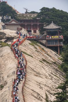 Huashan, China -  August 2019 : Crowds of tourists walking on a narrow ridge on a mountain trail to the West Peak on Huashan mountain, Xian, Shaanxi Province