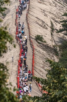 Huashan, China -  August 2019 : Crowds of tourists walking on a narrow ridge on a mountain trail to the West Peak on Huashan mountain, Xian, Shaanxi Province