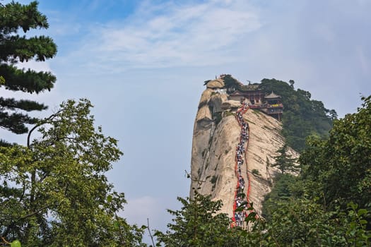 Huashan, China -  August 2019 : Crowds of tourists walking on a narrow ridge on a mountain trail to the West Peak on Huashan mountain, Xian, Shaanxi Province