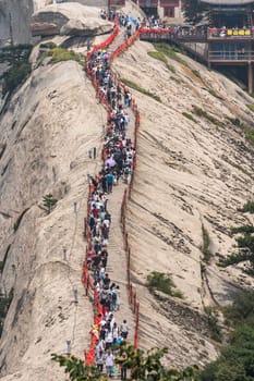 Huashan, China -  August 2019 : Crowds of tourists walking on a narrow ridge on a mountain trail to the West Peak on Huashan mountain, Xian, Shaanxi Province