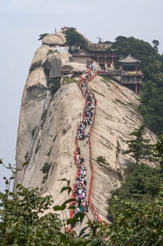 Huashan, China -  August 2019 : Crowds of tourists walking on a narrow ridge on a mountain trail to the West Peak on Huashan mountain, Xian, Shaanxi Province