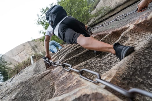 Huashan, China -  August 2019 : Tourist with backpack climbing up the steep, cut into rocky edge stairs on a mountain trail to the North and West Peak on Huashan mountain, Xian, Shaanxi Province