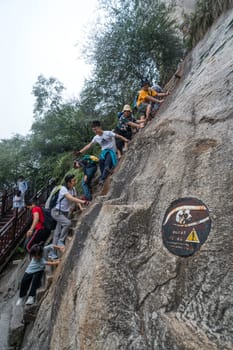 Huashan, China -  August 2019 : Tourists climbing up the vertical, steep, cut into rocky edge stairs on a mountain trail to the North and West Peak on Huashan mountain, Xian, Shaanxi Province