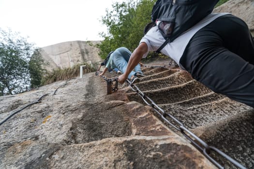 Huashan, China -  August 2019 : Tourist with backpack climbing up the steep, cut into rocky edge stairs on a mountain trail to the North and West Peak on Huashan mountain, Xian, Shaanxi Province