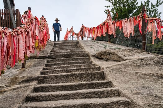 Huashan, China -  August 2019 : Male tourist with a hat walking down on the cut in a rock stone stairs steps leading to the summit of a West Peak on Huashan mountain, Xian, Shaanxi Province
