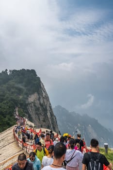 Huashan, China -  August 2019 : Crowds of tourists walking on a narrow ridge on a mountain trail to the West Peak on Huashan mountain, Xian, Shaanxi Province