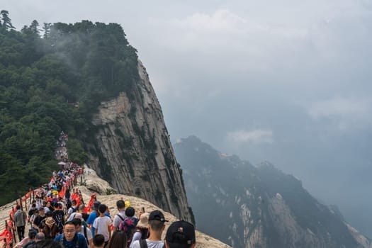 Huashan, China -  August 2019 : Crowds of tourists walking on a narrow ridge on a mountain trail to the West Peak on Huashan mountain, Xian, Shaanxi Province