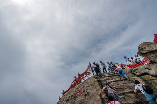 Huashan, China -  August 2019 : Crowds of tourists walking on a mountain trail to the summit of a West Peak on Huashan mountain, Xian, Shaanxi Province