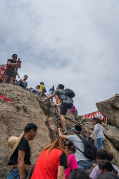 Huashan, China -  August 2019 : Crowds of tourists walking on a mountain trail to the summit of a West Peak on Huashan mountain, Xian, Shaanxi Province