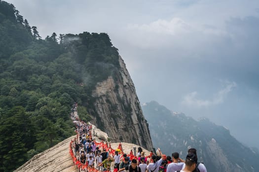 Huashan, China -  August 2019 : Crowds of tourists walking on a narrow ridge on a mountain trail to the West Peak on Huashan mountain, Xian, Shaanxi Province
