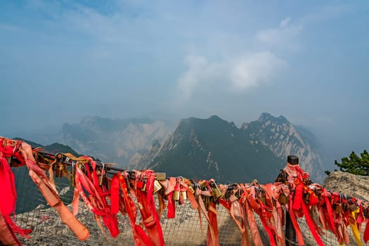 Huashan, China -  August 2019 : Red and yellow ribbons attached to the protective barrier on a lookout with the stunning mountain landscape view from the summit of West Peak, Huashan mountain, Shaanxi Province