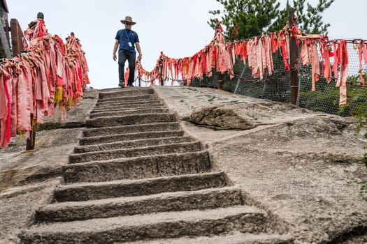 Huashan, China -  August 2019 : Male tourist with a hat walking down on the cut in a rock stone stairs steps leading to the summit of a West Peak on Huashan mountain, Xian, Shaanxi Province
