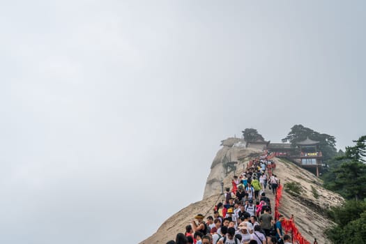 Huashan, China -  August 2019 : Crowds of tourists walking on a narrow ridge on a mountain trail to the West Peak on Huashan mountain, Xian, Shaanxi Province