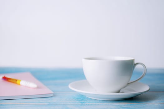 A cup of coffee with notebook on wooden blurred background