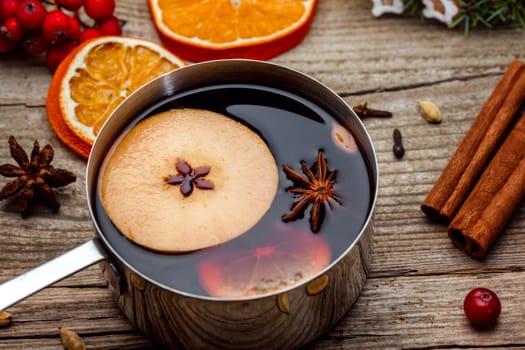 Small stewpot with mulled wine and cinnamon sticks, slice of oranges and apple on wooden table top view. Hot winter drink. Christmas beverage.