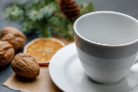 White cup and saucer on a Christmas background with walnuts, a slice of orange, with shallow depth of field