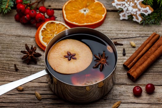 Small stewpot with mulled wine and cinnamon sticks, slice of oranges and apple on wooden table top view. Hot winter drink. Christmas beverage.