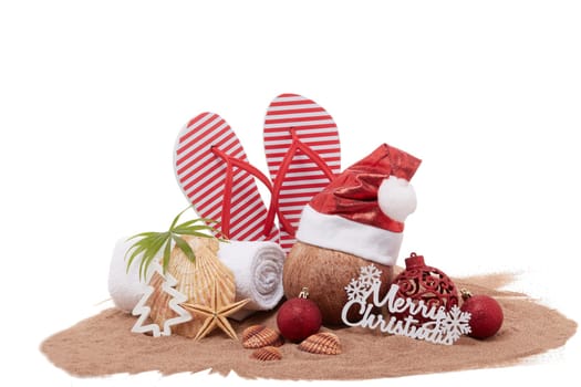 Still life with beach accessories (flip flops, towel, seashells, sand, coconut) and christmas ornaments on white background. Christmas. Winter vacation in warm countries, beach holiday