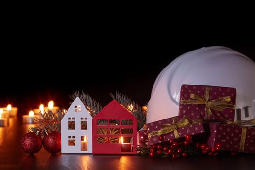 White construction hard hat, candles, gift boxes, fir branch and Christmas ornament on black background. Construction New Year, Christmas background with copy space. For greeting card or advertising